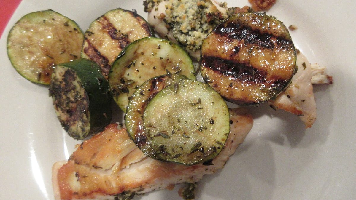 Dada ayam panggang berbumbu pesto bersama irisan zukini bakar bergaris panggangan di atas piring