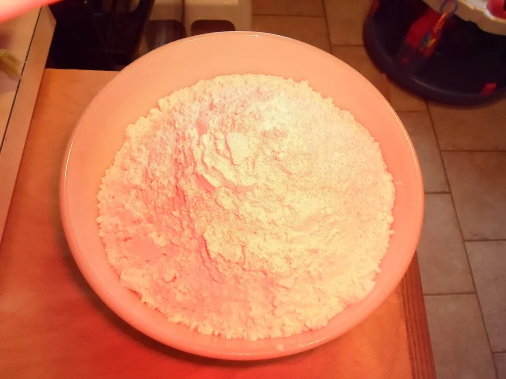 Tepung putih ditumpuk di dalam mangkuk pencampur berwarna merah muda.