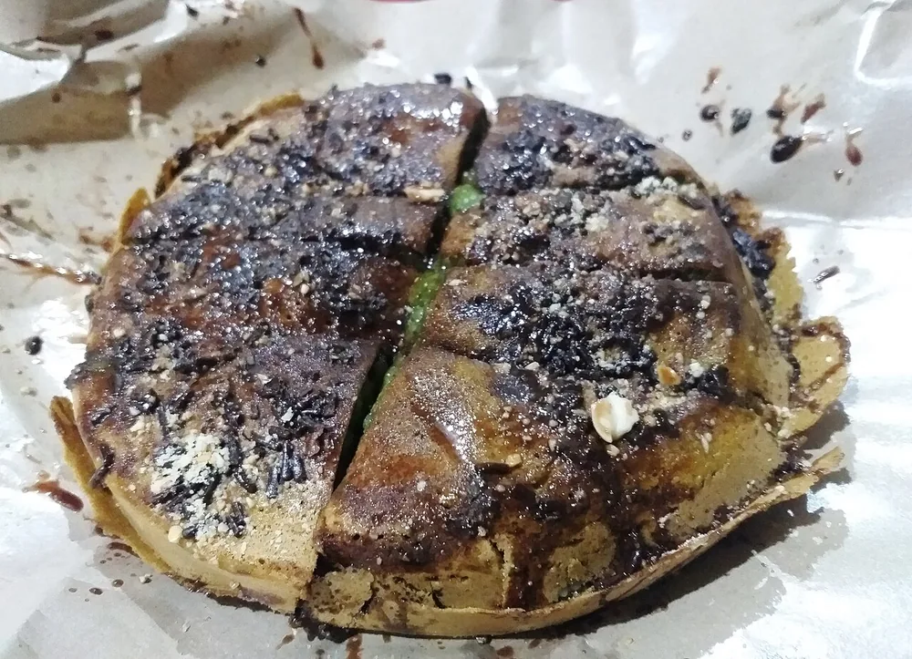 Martabak manis terbuka dengan taburan cokelat dan kacang, dipotong menjadi beberapa bagian.