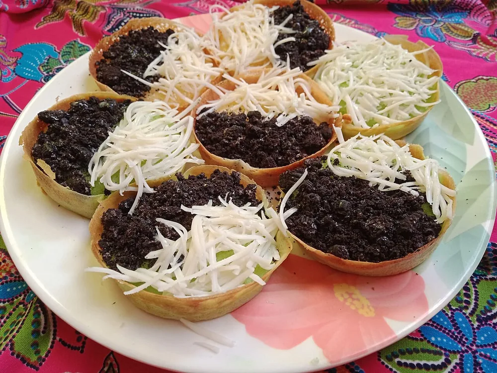 Beberapa martabak mini dengan taburan keju parut dan cokelat di atas piring bermotif bunga.