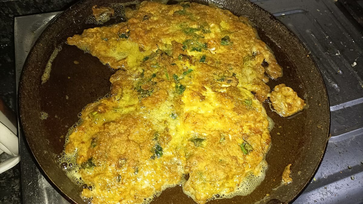 Telur dadar kuning keemasan bertabur irisan daun hijau yang sedang digoreng dalam wajan berminyak