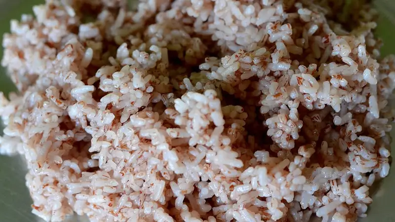 Nasi beras merah yang sudah matang dengan butiran berwarna merah muda kecokelatan, difoto dari dekat.