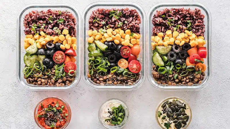 Tiga wadah kaca meal prep berisi nasi merah, jagung, tomat ceri, timun, zaitun, dan kacang lentil dengan porsi tertata