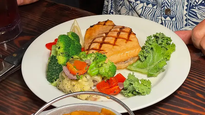 Sepiring salmon panggang dengan brokoli, paprika merah, wortel, dan selada keriting di atas meja makan