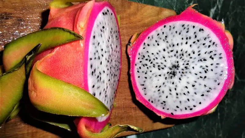 Buah naga berkulit merah muda yang dibelah dua, memperlihatkan daging buah putih berbiji hitam di atas talenan kayu.