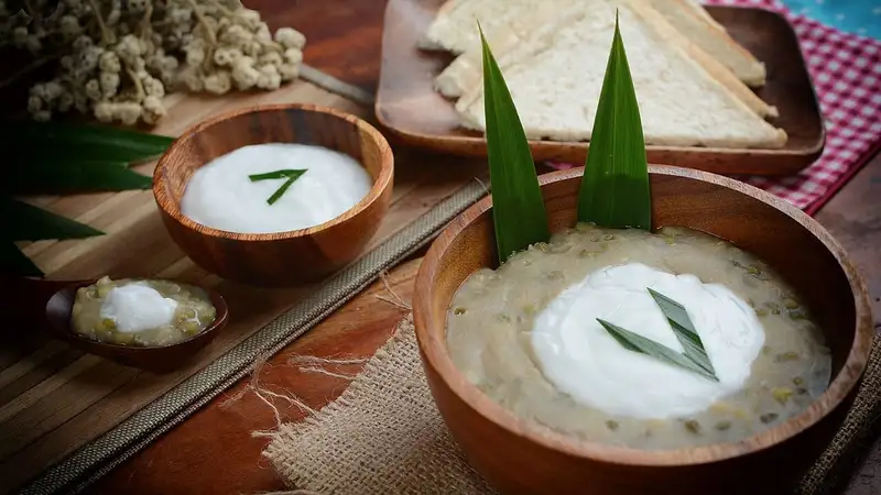 Bubur kacang hijau dengan siraman santan dan hiasan daun pandan dalam mangkuk kayu, ditemani roti tawar