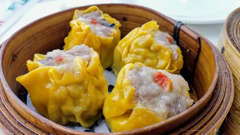 Empat siomay dimsum berkulit kuning dengan isian daging di dalam keranjang kukus bambu.