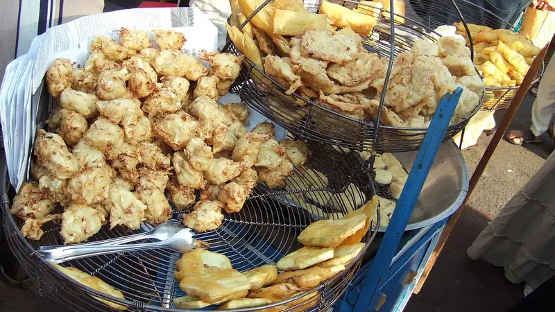 Aneka gorengan seperti bakwan, tempe, dan pisang goreng menumpuk di atas saringan kawat pada gerobak penjual gorengan