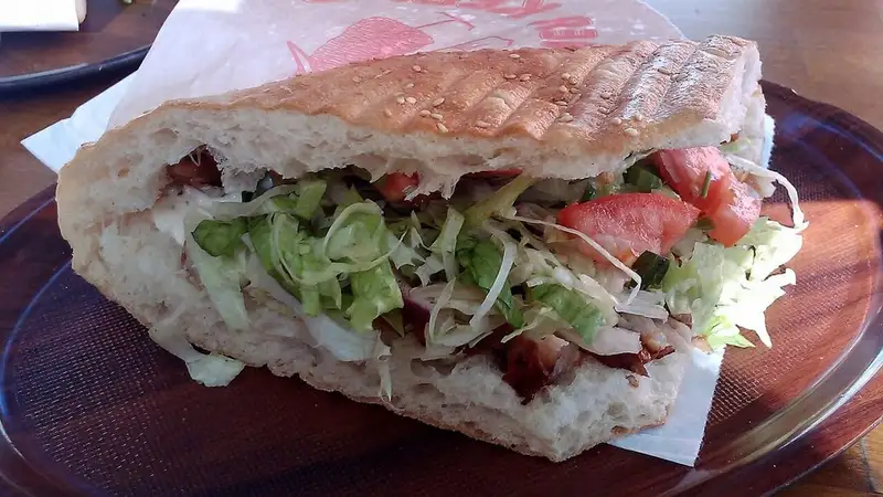 Kebab döner dalam roti pita panggang berisi irisan daging, kol, selada, dan tomat di atas kertas pembungkus.