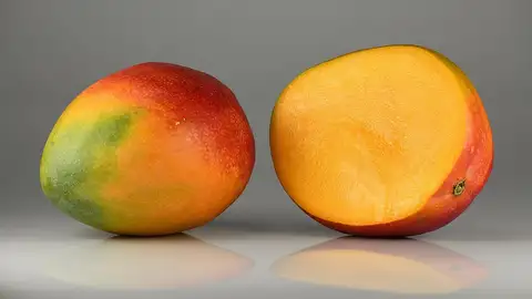 Dua buah mangga matang berkulit merah kehijauan, satu utuh dan satu dibelah memperlihatkan daging buah jingga