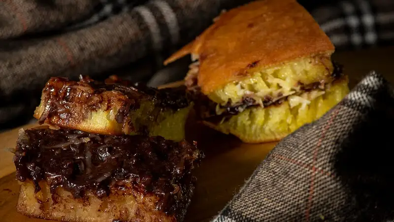Potongan martabak manis bertekstur berongga dengan isian cokelat meleleh, ditumpuk di atas kain bermotif kotak.