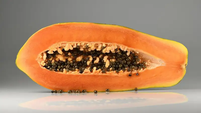 Sebuah pepaya matang dibelah memanjang, memperlihatkan daging buah oranye dan biji hitam di bagian tengah.