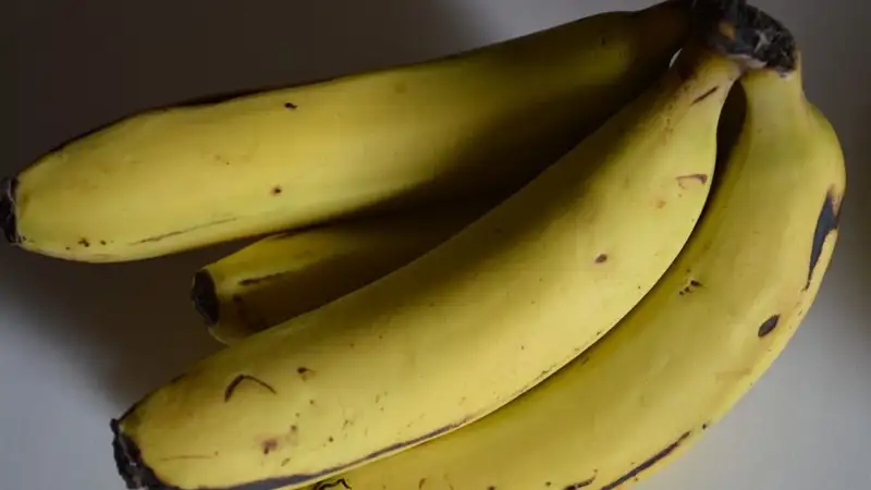 Satu sisir pisang kuning matang dengan bintik cokelat kecil pada kulitnya, diletakkan di atas permukaan meja.