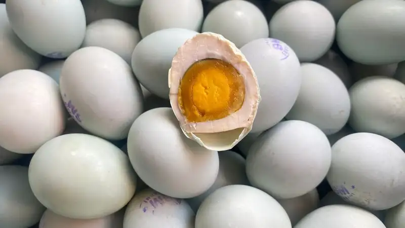 Tumpukan telur bebek asin bercangkang hijau kebiruan, salah satunya terbuka memperlihatkan kuning telur berwarna jingga.