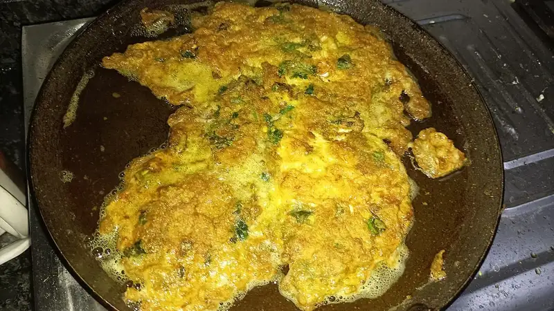Telur dadar kuning keemasan bertabur irisan daun hijau yang sedang digoreng dalam wajan berminyak