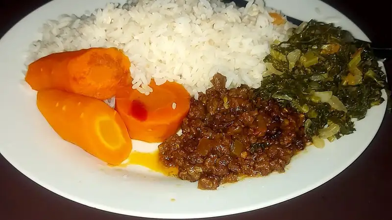 Sepiring makan siang berisi nasi putih, wortel rebus, sayur hijau tumis, dan lauk daging berbumbu.
