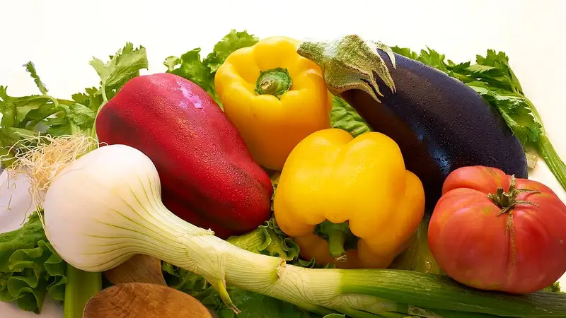 Aneka sayuran segar seperti paprika merah dan kuning, terung ungu, tomat, daun bawang, dan seledri tersusun berdampingan.