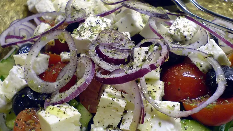 Salad Yunani berisi tomat, irisan bawang merah, zaitun hitam, dan potongan keju feta bertabur oregano