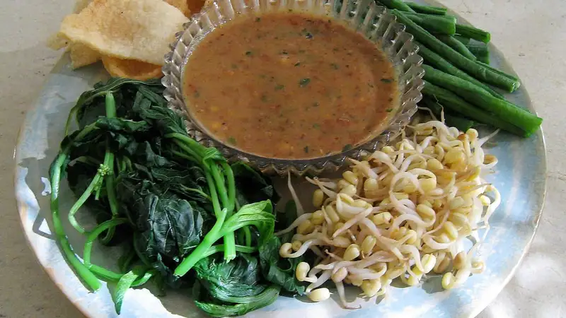 Sepiring pecel berisi bayam rebus, tauge, dan kacang panjang dengan semangkuk bumbu kacang serta peyek di tepi piring