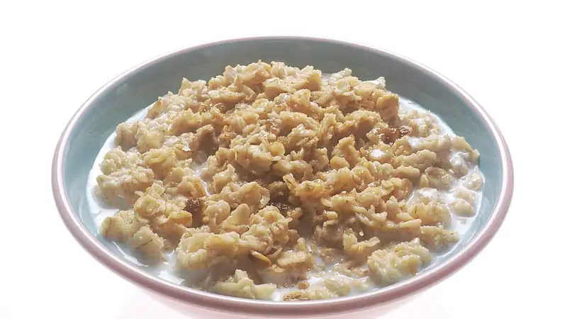 Semangkuk oatmeal matang dari serpihan gandum oat yang disiram susu, tersaji di mangkuk dengan latar putih.