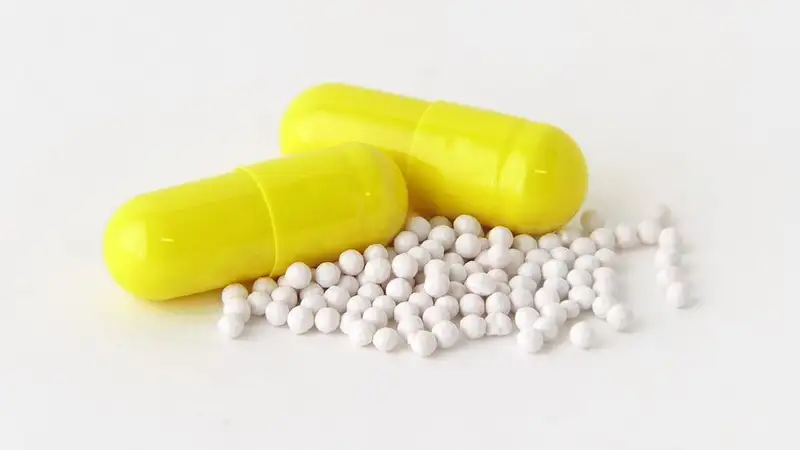 Dua kapsul omeprazol berwarna kuning dengan butiran pelet putih dari kapsul yang dibuka, di atas latar putih