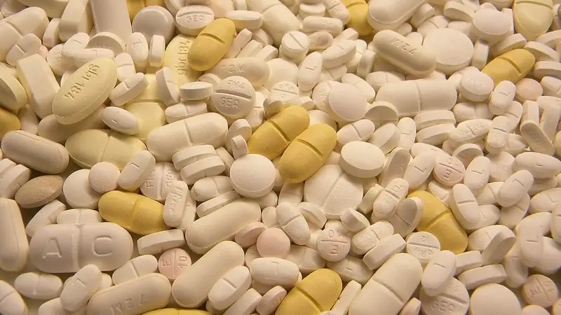 Tumpukan tablet obat berbagai bentuk, sebagian besar putih dan beberapa kuning, dilihat dari dekat.