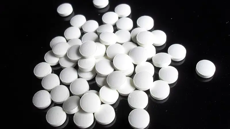 Butiran tablet obat bulat berwarna putih tanpa kemasan berserakan di atas permukaan hitam mengilap.