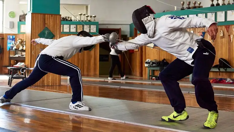 Dua pemain anggar bermasker beradu pedang epee di atas lintasan latihan sebuah klub anggar berlantai kayu