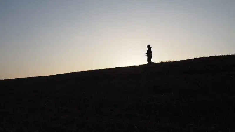 Siluet seorang pelari yang sedang jogging di puncak tanggul berumput dengan latar langit senja yang terang