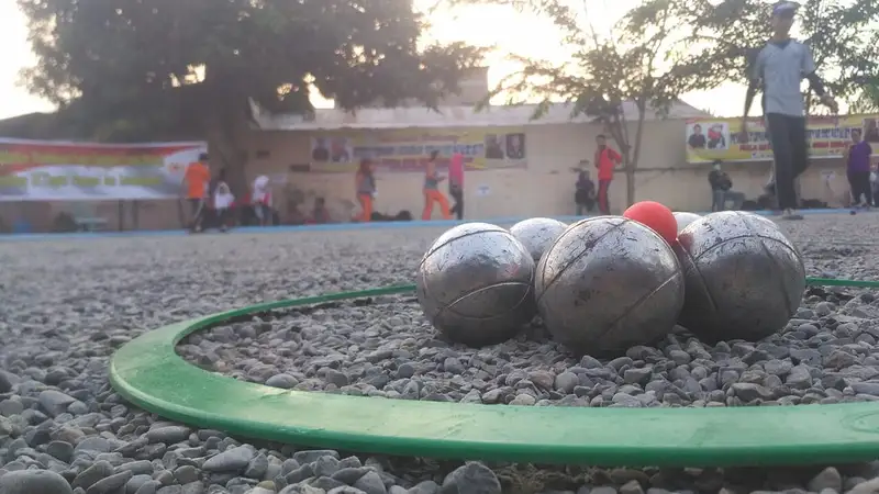 Beberapa bola besi petanque dan bola sasaran merah di dalam lingkaran lempar hijau di lapangan kerikil saat kejuaraan pelajar.