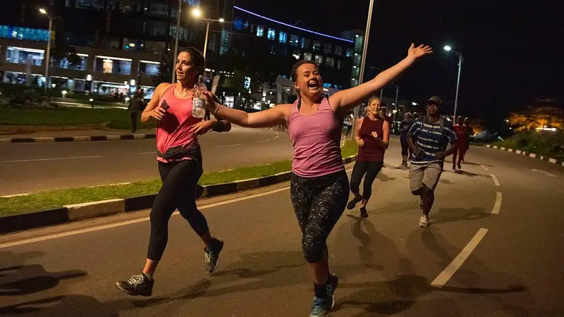 Sekelompok orang berlari dan berolahraga bersama di jalan raya pada malam hari di bawah lampu jalan.