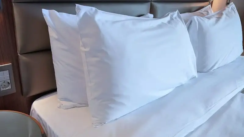 Beberapa bantal putih ditumpuk bersandar pada kepala ranjang di atas kasur berseprai putih