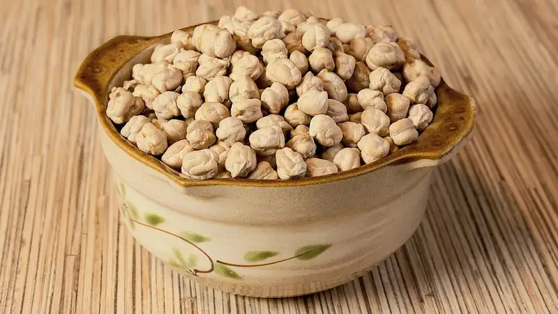 Kacang arab (chickpea) kering memenuhi mangkuk keramik bermotif daun di atas alas anyaman bambu