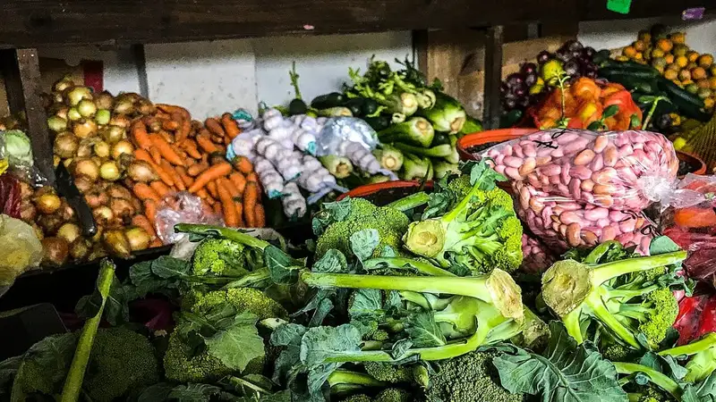 Aneka sayuran segar seperti brokoli, wortel, bawang bombai, bawang putih, dan kacang merah tertata di lapak pasar.