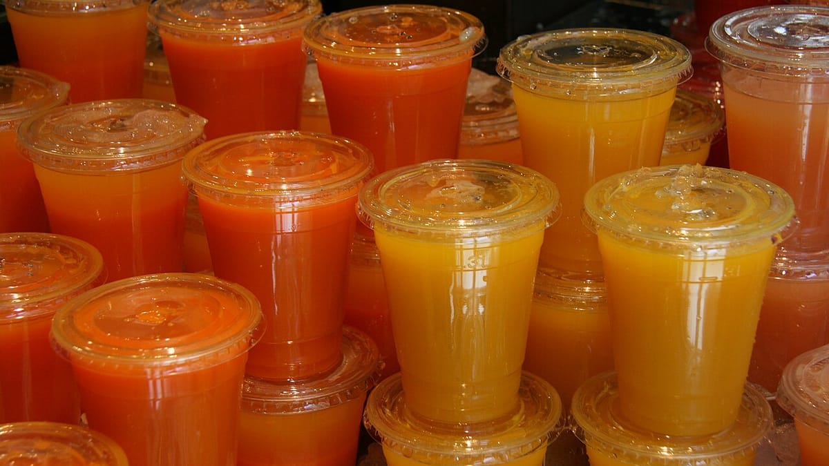 Deretan gelas plastik bertutup berisi jus buah berwarna jingga, kuning, dan merah yang dijajakan di kios minuman