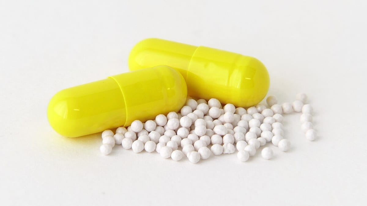 Dua kapsul omeprazol berwarna kuning dengan butiran pelet putih dari kapsul yang dibuka, di atas latar putih