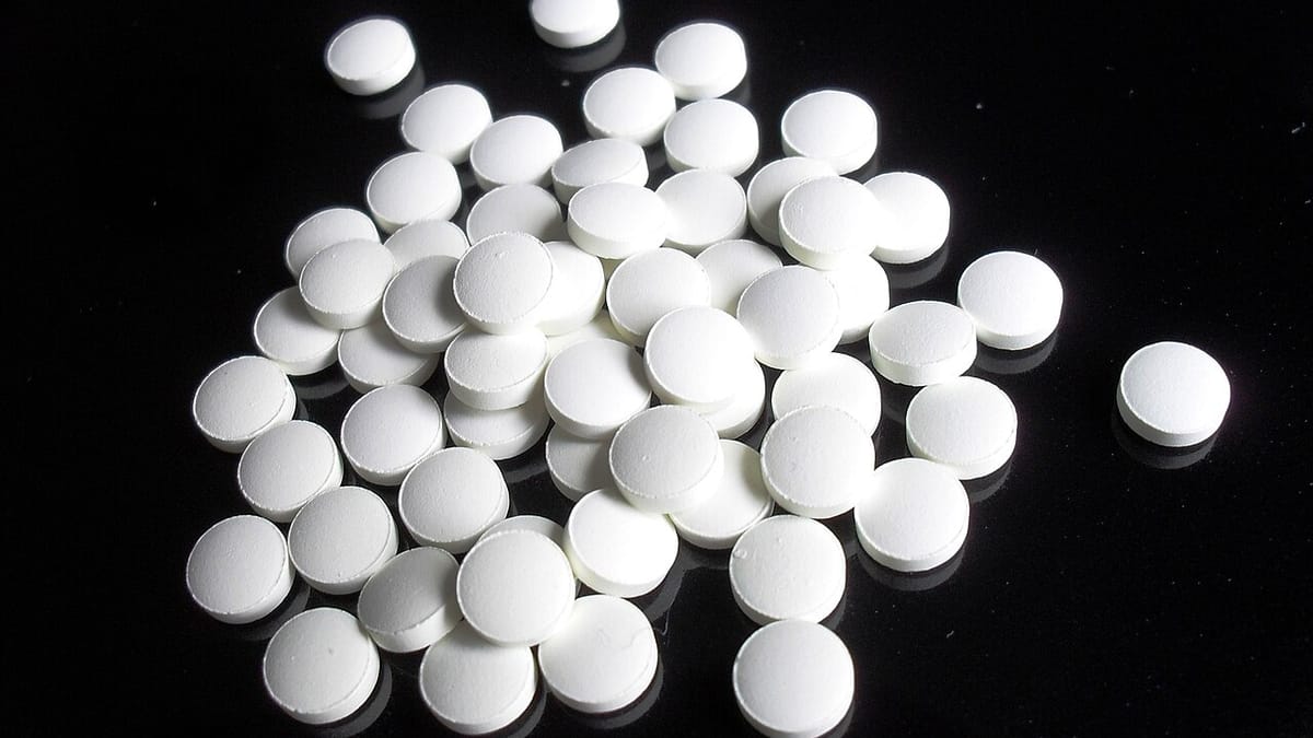 Butiran tablet obat bulat berwarna putih tanpa kemasan berserakan di atas permukaan hitam mengilap.
