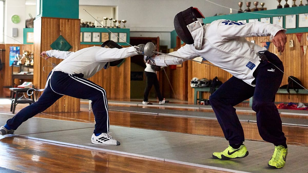 Dua pemain anggar bermasker beradu pedang epee di atas lintasan latihan sebuah klub anggar berlantai kayu