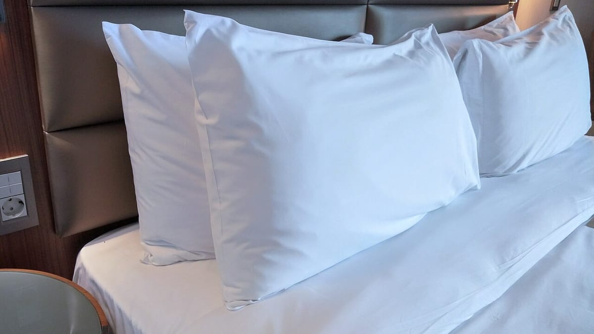 Beberapa bantal putih ditumpuk bersandar pada kepala ranjang di atas kasur berseprai putih