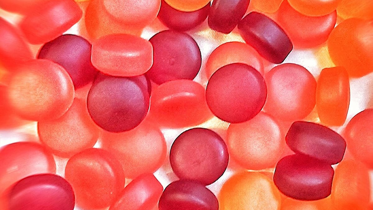 Tumpukan vitamin gummy berwarna merah dan jingga yang tembus cahaya, difoto dari dekat