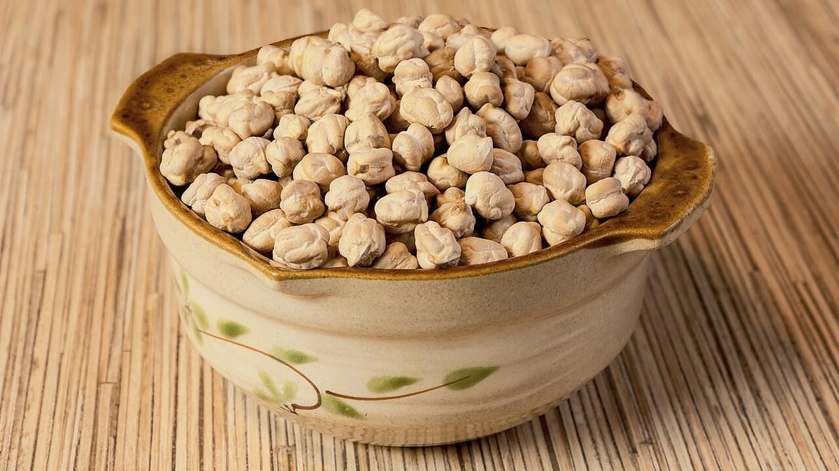 Kacang arab (chickpea) kering memenuhi mangkuk keramik bermotif daun di atas alas anyaman bambu
